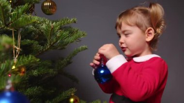 Mutlu küçük kız Noel ağacını taşaklarla süslüyor.