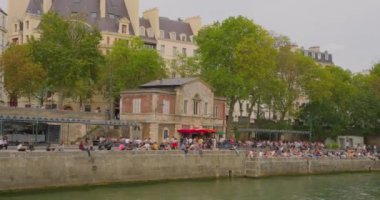 Fransa, Paris, 01 Ağustos 2023: Paris, Fransa 'da Siene nehri kıyısında oturan Parisliler. Nehirden geçen bir geminin setin manzarası. Yüksek kalite 4k görüntü