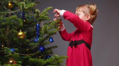 Mutlu küçük kız Noel ağacını taşaklarla süslüyor.