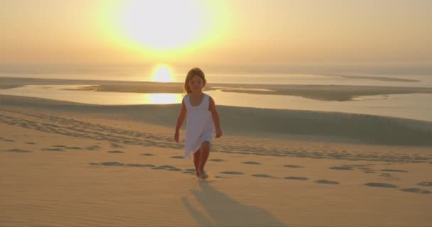Красивая Маленькая Девочка Белом Платье Ходит Босиком Песку Золотом Закате — стоковое видео