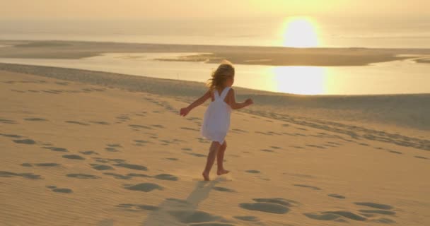 Красивая Маленькая Девочка Белом Платье Бежит Босиком Песку Золотом Закате — стоковое видео