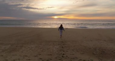 Gün batımında okyanus kıyısında çıplak ayakla koşan bir kadının silueti. Doğayla bütünlük kavramı.