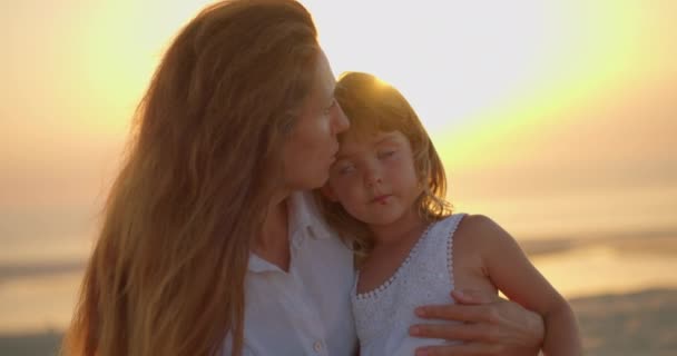 若い母親は日没時に太陽の下の海で小さな娘を抱きしめている 家族関係の緊張 家族愛の概念 幸せな家族 — ストック動画