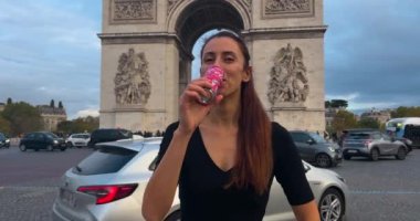 Fransa 'nın başkenti Paris' teki Zafer Takı 'nın arka planına karşı olimpiyatlarla ilgili reklamı olan Coca Cola içen bir kız. Coca Cola, Paris 'te düzenlenen 2024 Yaz Olimpiyatları' na sponsor oldu..