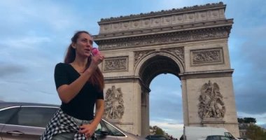 Fransa, Paris, 30 Ağustos 2023: Bir kız Arc de Triomphe 'nin arka planına karşı olimpiyatlarla ilgili bir reklamı olan Coca Cola içiyor. Coca Cola, Paris 'te düzenlenen 2024 Yaz Olimpiyatları' na sponsor oldu..