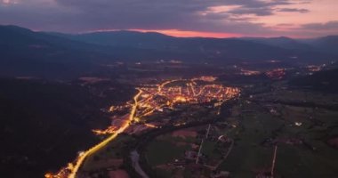 Geceleri dağlardaki bir şehrin yüksek hızda görüntüsü. Sokak lambalarının ışığında arabalar şehirde hareket ediyor..
