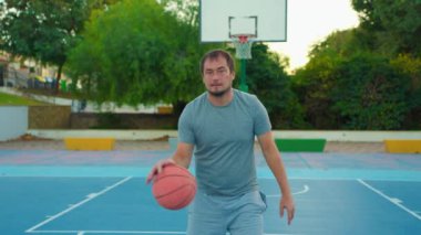 Sporcu dışarıda sahada topla oynuyor. Basketbol potasının arka planında duran ve kameraya bakan adamın portresi. Yavaş çekim sokak basketbolu.