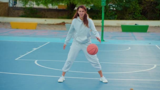 地元の裁判所で女性バスケットボール選手のトレーニングと屋外での運動の映像を閉じます 若い女性はバスケットボールボールとバウンスクロスをトレーニングします スローモーションストリートバスケットボール — ストック動画