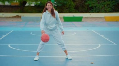 Kadın basketbol oyuncusunun yerel sahada antrenman ve egzersiz yaptığı görüntüleri kapatın. Basketbol topuyla çapraz atlama eğitimi alan genç bir kadın. Yavaş çekim sokak basketbolu.
