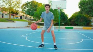 Genç basketbol oynar. Sağlıklı bir yaşam tarzı. Moda tarzı saçı olan bir adam kameraya bakar ve basketbol topuyla oynar. Okuldan sonra açık havada bir gencin portresi..