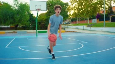 Genç basketbol oynar. Sağlıklı bir yaşam tarzı. Moda tarzı saçı olan bir adam kameraya bakar ve basketbol topuyla oynar. Okuldan sonra açık havada bir gencin portresi..