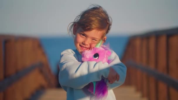 소녀가 좋아하는 장난감을 포옹합니다 아이는 분홍색 유니콘으로 연주하고 자신의 키스와 — 비디오
