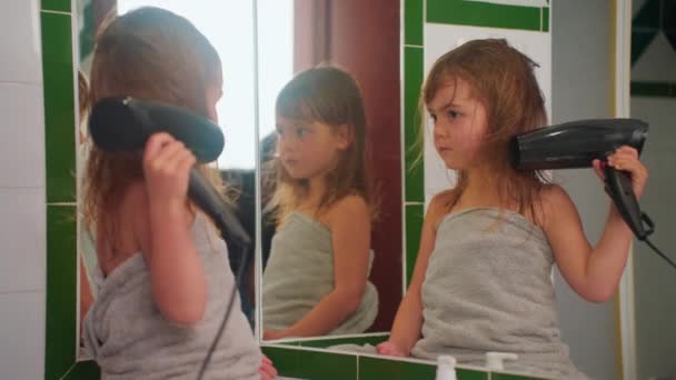 かわいい少女は 鏡の近くに座っているシャワーの後 ヘアドライヤーで彼女自身を乾かします — ストック動画