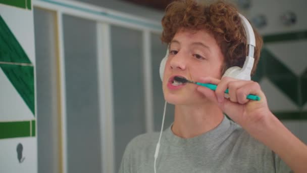 Nastolatek Kręconymi Włosami Wykonuje Codzienną Rutynę Mycia Zębów Słuchawkami Śpiewania — Wideo stockowe