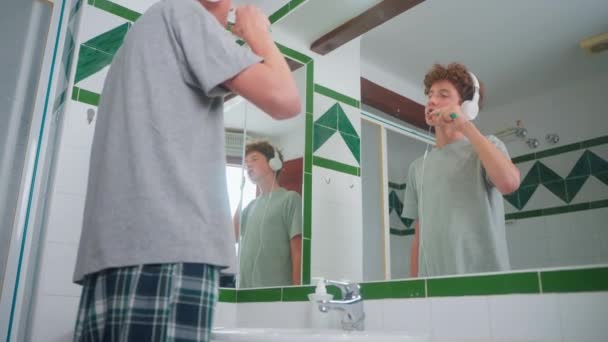 头发卷曲的青少年每天用耳机刷牙 用牙刷唱歌 — 图库视频影像