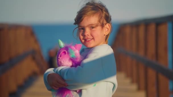 小さな女の子は彼女のお気に入りの玩具を抱きしめている 子供はピンクのユニコーンで遊んでいる 赤ちゃんの手の柔らかいおもちゃ — ストック動画
