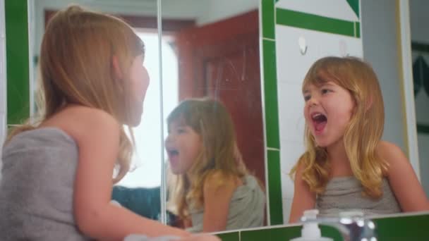 漂亮的小女孩穿着毛巾坐在镜子前的浴室里 看着自己 嬉笑着玩耍 — 图库视频影像