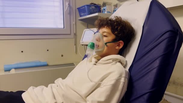 生病的少年在医院里带着吸入器 一个不健康的孩子在医院里吸气 青少年呼吸时戴上氧气面罩以减轻病程 — 图库视频影像