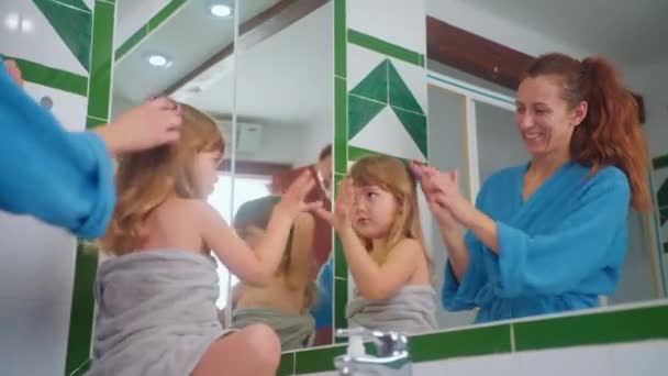 幸せな母親は 彼女の小さなかわいい娘の髪を鏡の前でコメディしています 子供と過ごした時間 チャイルドケア — ストック動画