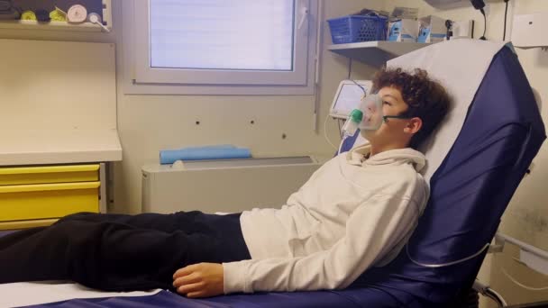 生病的少年在医院里带着吸入器 一个不健康的孩子在医院里吸气 青少年呼吸时戴上氧气面罩以减轻病程 — 图库视频影像