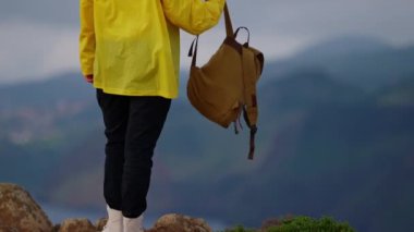 Yolculuk için beyaz yürüyüş botları. Kamera bir kadını gezide ya da macerada takip eder. Genç gezgin ya da seyahat blogcusu güzel dağ vadisinde yürüyor. Sırt çantalı, sarı yağmurluklu bir kadın yürüyüşçü..