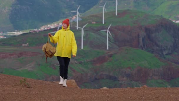 旅行のためのホワイトハイキングブーツ カメラは 旅行や冒険に女性をフォローしています 若い旅行者や旅行ブロガーは美しい山の谷を歩いています バックパック付き黄色いレインコートの女性ハイカー — ストック動画
