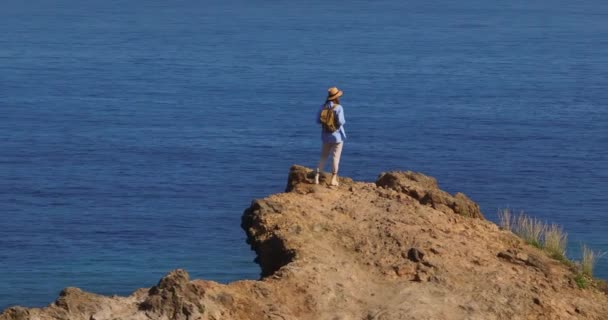 旅人は楽園の島を歩いている アクティブな若い女性は 春のハイキングでハイキングや登山ブーツや履物を見るために崖の上に登ります — ストック動画