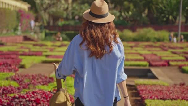 マデイラ島とファチュアルシティの多様な植生を持つランドマークガーデンを訪れる旅行者 植物園のカラフルな花の間を歩く帽子とバックパックを持つ女性 — ストック動画