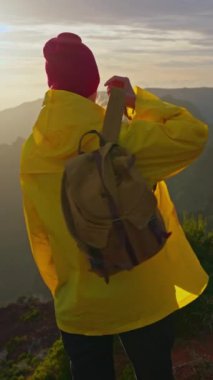 Ağır çekim kamera, sırt çantalı, sarı yağmurluklu kadını takip ediyor. Sırt çantasıyla gezen çekici, mutlu bir genç kız. Madeira adasının dağlarında güneş ufukta batıyor..