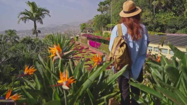 マデイラ島とファチュアルシティの多様な植生を持つランドマークガーデンを訪れる旅行者 植物園のカラフルな花の間を歩く帽子とバックパックを持つ女性 — ストック動画
