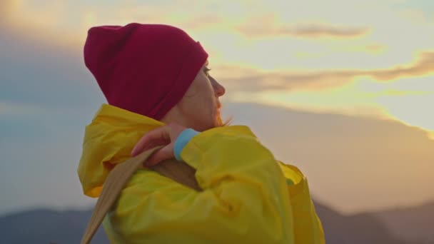 スローモーションカメラは バックパック付きの黄色いレインコートの女性ハイカーに続きます バックパックハイキングの魅力的な幸せな若い女の子 マデイラ島の山々の地平線に太陽を設定する — ストック動画