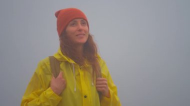 Sarı yağmurluk giymiş, sisli bir kadın gezgin doğa ve hayatın tadını çıkarıyor. Seyahat, yolculukta macera. Yaşam tarzı konsepti. Sarı kabarık ceketli yolcu..