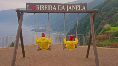 Ribera de Janela 'daki salıncaktan bir çift turist Portekiz' in Seixal Madeira köyünü inanılmaz bir şekilde görüyorlar..