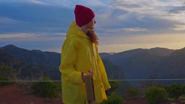 女性の旅行者は日没で山の頂上に登って景色を楽しんだ後 肩にバックパックを投げます — ストック動画