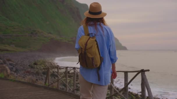 ハッピーな若い女性の観光客は 展望デッキ上の帽子とバックパックで海を歩いて 最高の景色を楽しんでいます マデイラ島 ポルトガル — ストック動画