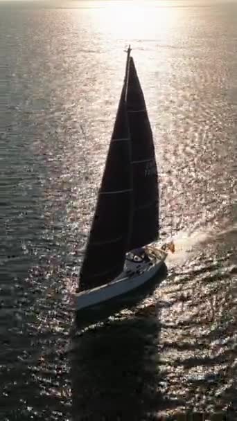 太陽の光線に帆で白いヨットの空中撮影を確立する 水の上に輝いている 青い海のセーリングヨットのシルエット ドローンからのショット — ストック動画