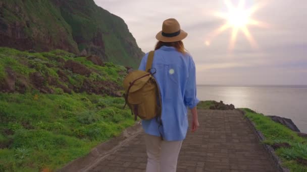 ハッピーな若い女性の観光客は 展望デッキの帽子とバックパックで海を散歩し 最も美しい夕日で最高の景色を楽しんでいます マデイラ島 ポルトガル — ストック動画