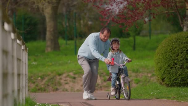 Маленькая Девочка Катается Велосипеде Парке Заботливым Отцом Который Учит Кататься — стоковое видео
