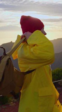 Ağır çekim kamera, sırt çantalı, sarı yağmurluklu kadını takip ediyor. Sırt çantasıyla gezen çekici, mutlu bir genç kız. Madeira adasının dağlarında güneş ufukta batıyor..