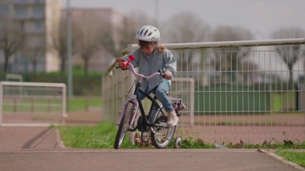 ヘルメットでかわいい軽い髪の少女は 通りの実際の自転車に乗ることを学びますが それでうまくいきません — ストック動画