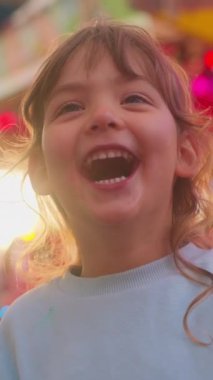 Gülmekten kırılmayan mutlu küçük kızın yakın plan portresi. Çocuk yakından gülüyor. Yüzü komik, dalgın bir çocuk. Dikey video.
