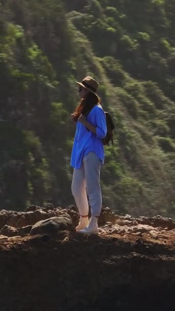 バーティカルビデオ 旅人は楽園の島を歩いている アクティブな若い女性は 春のハイキングでハイキングや登山ブーツや履物を見るために崖の上に登ります 高品質のフルHd映像 — ストック動画