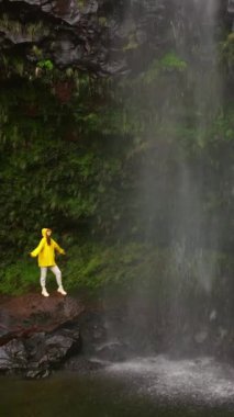 Dikey video. Şelale altında kollarını açmış, doğa macerasında yürüyüş yapan bir kadının hava manzarası. Seyahat, özgürlük ya da yolculuk.