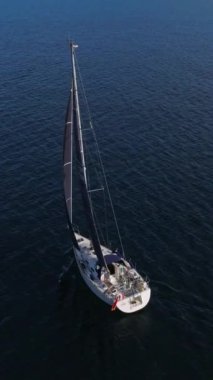 Batan güneşin ışınlarında yelkenli beyaz bir yatın hava görüntüsünü ayarlıyorum. Suyun üstünde parla. Mavi denizde yüzen bir yatın silueti. İHA 'dan ateşlenmiş..