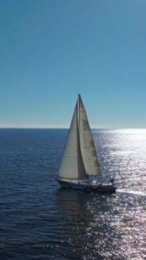 Açık okyanus derin mavi denizinde yüzen bir yatın insansız hava aracı videosu. Açık denizde yelkenli yatlı güneş deniz manzarası. Okyanus körfezinde yelkenlilerle açılmak. Güneşli yaz gününde lüks yat hayatı..