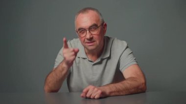 Yaşlı, tatminsiz, gri tişörtlü, uyarı işareti yapan, hayır diyen ve geri çekilme tavsiyesi vermekle tehdit eden bir adam..