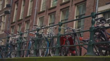 Kanal boyunca turist teknesi, köprüsü ve eski evleri bulunan Amsterdam manzaralı kanalı kuruluyor. İnsanlar bisiklet ve elektrikli tekne kullanıyor..