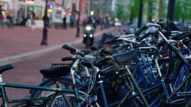 Kanal boyunca turist teknesi, köprüsü ve eski evleri bulunan Amsterdam manzaralı kanalı kuruluyor. İnsanlar bisiklet ve elektrikli tekne kullanıyor..