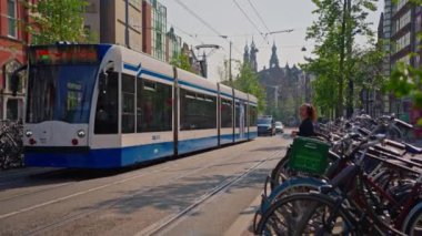 Amsterdam, Hollanda, 09 Haziran 2024: Kanal boyunca geçen turist teknesi, köprüsü ve eski evleri ile Amsterdam manzaralı şehir manzaralı bir kanalın kuruluşu. İnsanlar bisiklet ve elektrikli tekne kullanıyor..