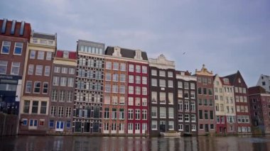 Kanal boyunca turist teknesi, köprüsü ve eski evleri bulunan Amsterdam manzaralı kanalı kuruluyor. İnsanlar bisiklet ve elektrikli tekne kullanıyor..